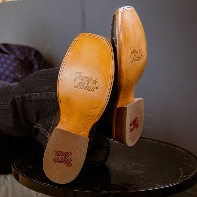 Man sitting on bench, wearing the Quaid Western Boots with Tony Lama logo on sole.